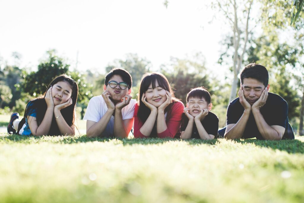 Asian family posing happily on the grass in a sunny park, showcasing love and togetherness.