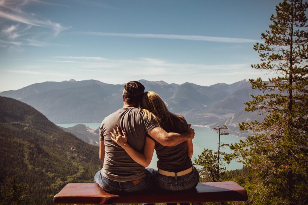 Couple sitting on bench embracing scenic mountain view, embodying romantic nature escape.