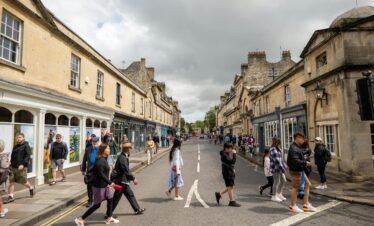 People walking through a vibrant street in Bath, UK, showcasing Georgian architecture and lively urban life.